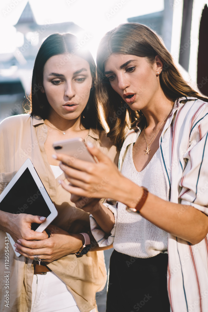 Poster amazed hipster girls watching web video impressed with received interesting facts, wonder female use