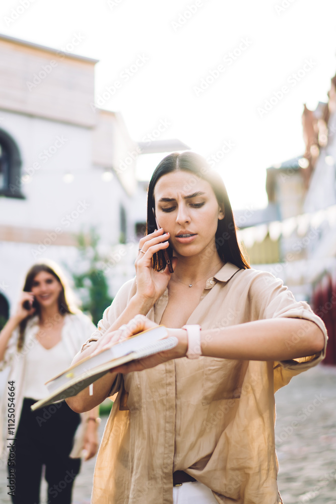 Poster puzzled female with textbook checking smartwatch time during international smartphone conversation, 