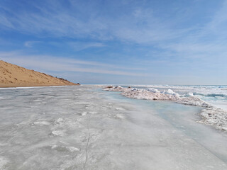 Frozen landscape showcases icy layers along a beach with ice chunks, emphasizing the contrast with the blue sky