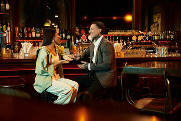 A multicultural couple enjoys drinks and laughter at a stylish bar on their night out.