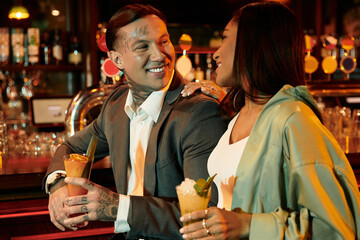 A young couple enjoys cocktails and each others company at a lively bar.