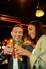 Tattooed couple toasting drinks at a vibrant bar, sharing smiles during their night out.