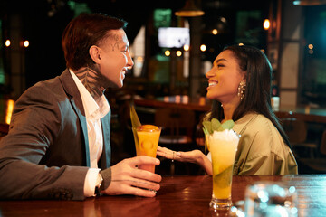 Tattooed young adults share laughter and drinks during a romantic evening at the bar.