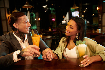 A young couple shares a special moment at the bar, sipping colorful cocktails and smiling.