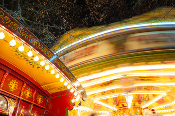 Brightly lit and spinning fun fair horse ride carousel seen on a winters night. A nearby wooden...