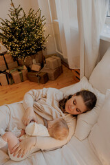 Mother breastfeeding baby on bed at christmas, vertical light photo