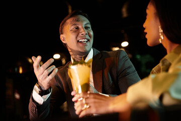 Multicultural couple shares laughter and drinks on a vibrant evening date at a bar.