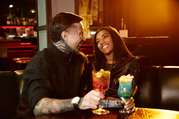 A young couple shares laughter and cocktails while on a delightful night out at a bar.