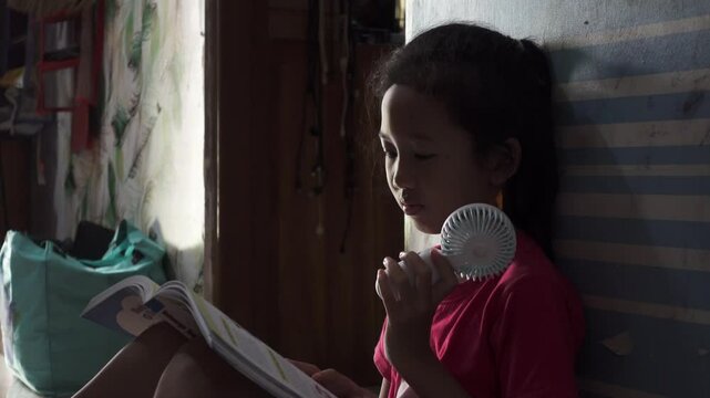 A girl reading the book on hot summer while holding a hand fan. Cool wind from portable fan at summer heat.