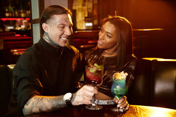 Young couple shares a joyful moment, sipping cocktails in a vibrant bar ambiance.