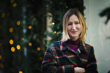 A close-up portrait of a woman surrounded by pine branches, her expression calm and thoughtful, blending natural textures with an urban atmosphere.