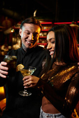 A multicultural couple shares laughter and drinks during a fun evening at the bar.