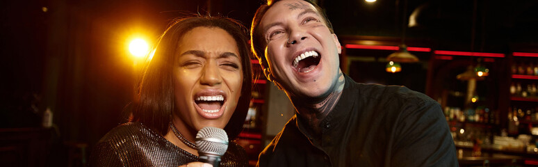 A young couple shares joyful moments while singing together at a lively bar during night out.