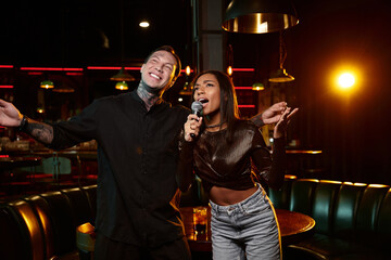 A young couple with tattoos shares a fun moment singing at a lively bar on a night out.