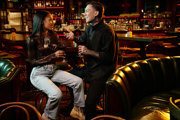 A tattooed couple shares smiles and drinks during a cozy evening in an upscale bar.