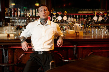A tattooed young man relaxes at the bar while soaking in the vibrant nightlife atmosphere.