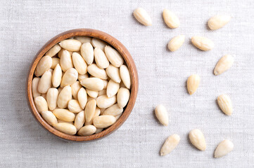 Blanched almonds in a wooden bowl on linen fabric. Shelled almonds, treated with hot water to remove the seed coat and reveal the seed. Fruits of Prunus amygdalus, used as snack or baking ingredient.
