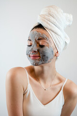 Young charm woman wear towel pampering face with mud or black clay facial mask isolated on grey