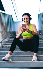 Smiling slim female runner satisfied with morning workout recording results on smartphone app, good...