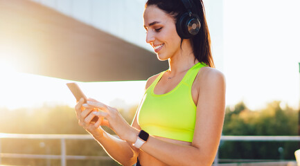 Happy millennial sport woman in electronic headphones checking mobile chatting on smartphone device...
