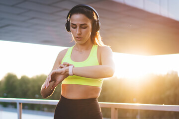 Young Caucasian female jogger in headphones enjoying music playlist using wearable device on wrist...