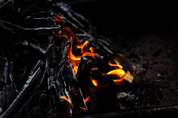 Orange fire and heat from burning firewood, glowing and burning, from charcoal, close-up at night with a dark background. Coziness from the fireplace atmosphere.