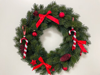 Traditional Christmas wreath decoration with red decoration hanging on white entrance door