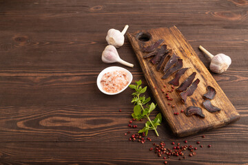 Armenian Basturma dried meat on wooden cutting board with pepper and herbs on brown wooden. Side view, copy space.