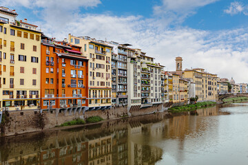 Colorful buildings reflect on the Arno River, showcasing Florence's rich history and stunning architecture. Visitors can enjoy the serene views along the waterfront.