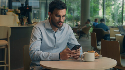 Arabian man ethnic muslim Indian businessman guy entrepreneur manager using mobile phone business lunch in cafe restaurant male visitor millennial tourist read message cellphone expect smartphone sms