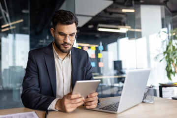 A business professional focuses on his tablet in a modern office setting, highlighting technology and productivity in the workplace.