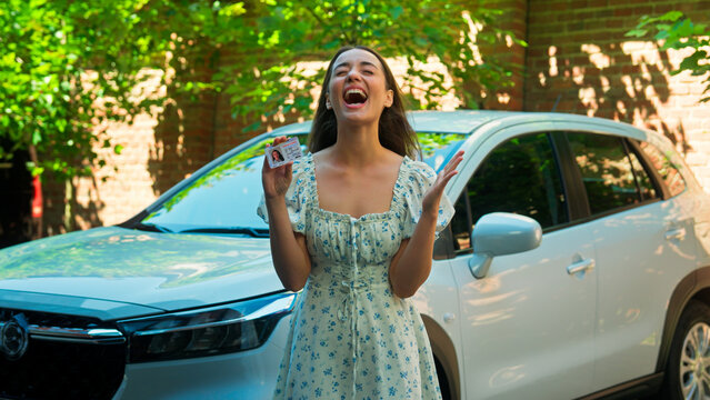 Happy excited amazed Caucasian woman female girl student client buyer buy new car automobile showing driver license successfully passed exam test driving lessons celebrating excitement at city street