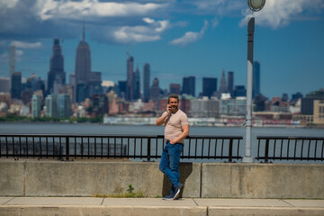 Man talking at the phone in New York City. Man talking on the phone on NY skyline. Man in t-shirt talking on cell phone. Guy talking by mobile phone. Tourist in city street holding smartphone.