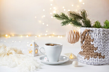 Cup of tea into a white table. Cozy Christmas decoration. Knitted basket with Christmas tree, ornament, plaid. Hygge warm atmosphere