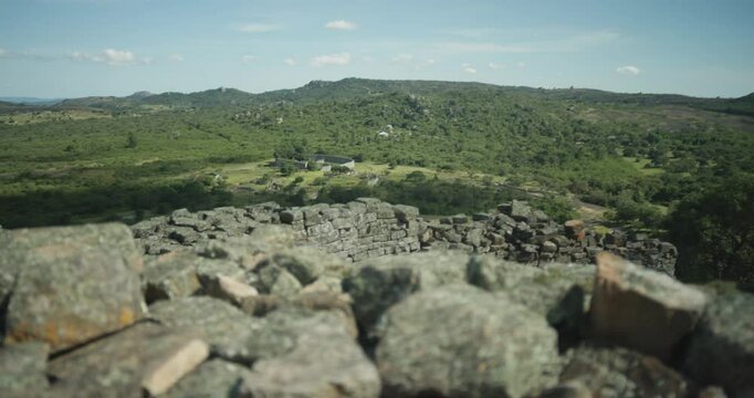 Slow motion establishing landscape of Great Zimbabwe national monument at ancient and historic African settlement ruins, including stone walls, lush trees, and hill complex