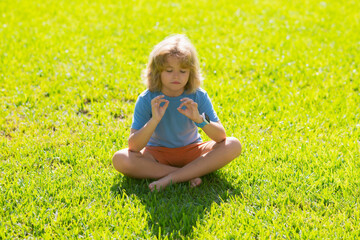 Child doing yoga pose in the park outdoor. Calmness and relax. Kid meditates while practicing yoga. Mindfulness meditation. Relaxed boy with closed eyes enjoying nature.