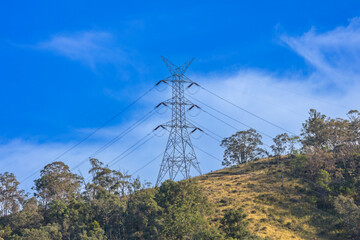 Photograph of a large electricity Transmission Tower on a grassy hill against a bright blue sky in...