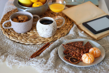 Books, e-reader, tea, orange juice, fruit, snacks, yarn, blanket and lit candles on the table....
