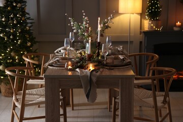 Christmas table setting with stylish dishware, glasses and burning candles in festive decorated room