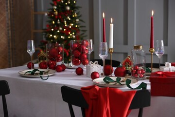 Christmas table setting with stylish dishware, glasses and burning candles in festive decorated room