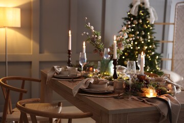 Christmas table setting with stylish dishware, glasses and burning candles in festive decorated room