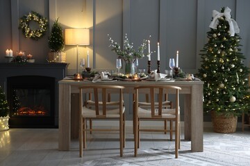 Christmas table setting with stylish dishware, glasses and burning candles in festive decorated room