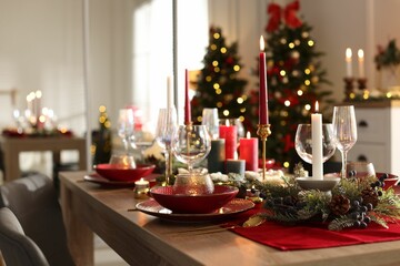 Christmas table setting with stylish dishware, glasses and burning candles in festive decorated room