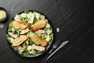 Delicious Caesar salad with chicken and cheese on black textured table, flat lay. Space for text