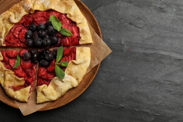 Tasty galette with strawberries, blueberries and mint on dark gray textured table, top view. Space for text
