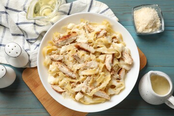 Tasty Alfredo pasta with chicken on light blue wooden table, flat lay