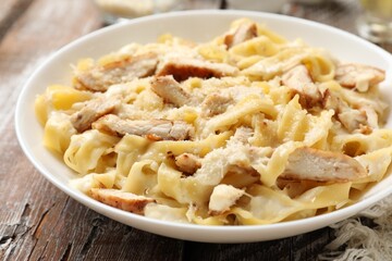Tasty Alfredo pasta with chicken on wooden table, closeup