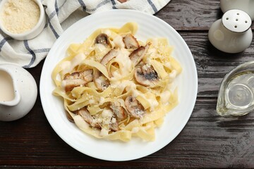 Tasty Alfredo pasta with chicken, mushrooms, cheese and creamy sauce on wooden table, flat lay