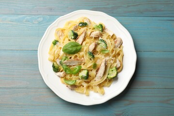 Delicious pasta Alfredo with chicken, cheese, broccoli and basil on light blue wooden table, top view