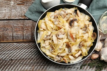 Flat lay composition with tasty Alfredo pasta with chicken and mushrooms in frying pan on wooden table, space for text